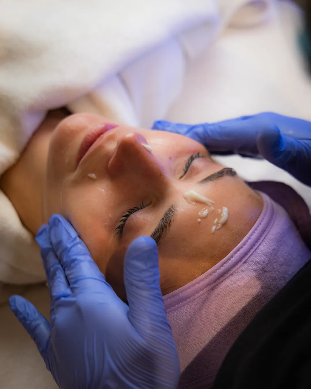 Des mains gantées massent le front pendant un soin du visage